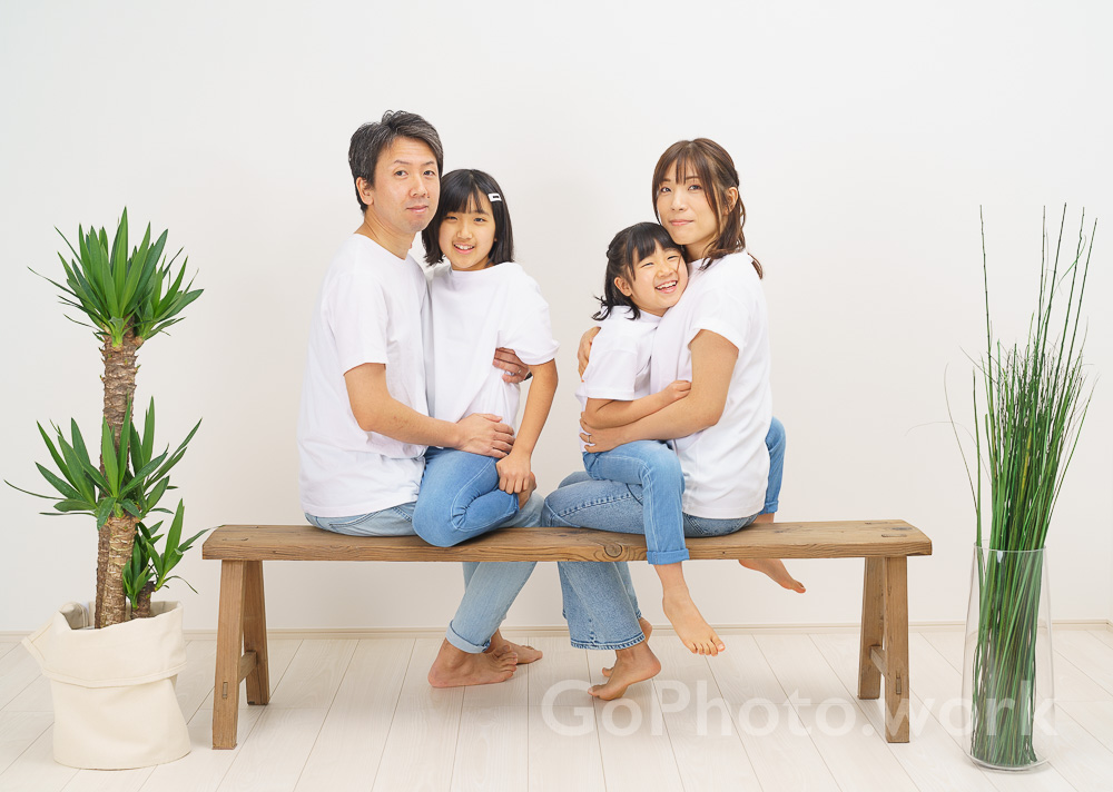 白いスタジオでベンチに座り撮影する家族