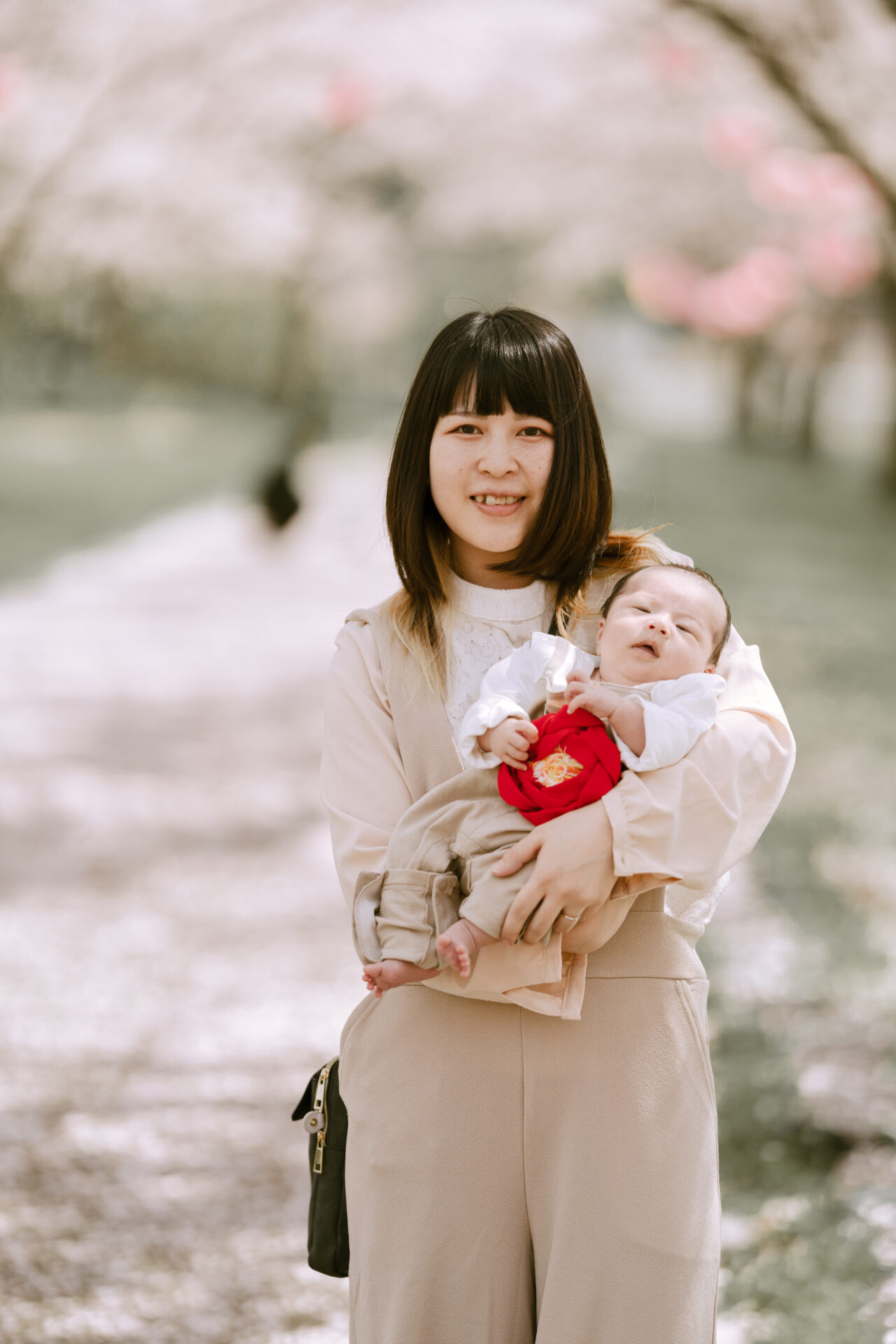 小松木場潟公園の満開の桜の樹の下で新生児を抱く母親