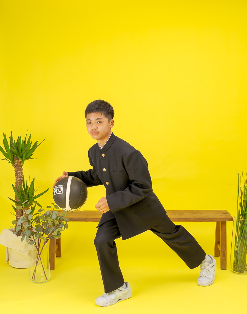 スタジオの黄色い背景紙で学生服を着てバスケをする写真