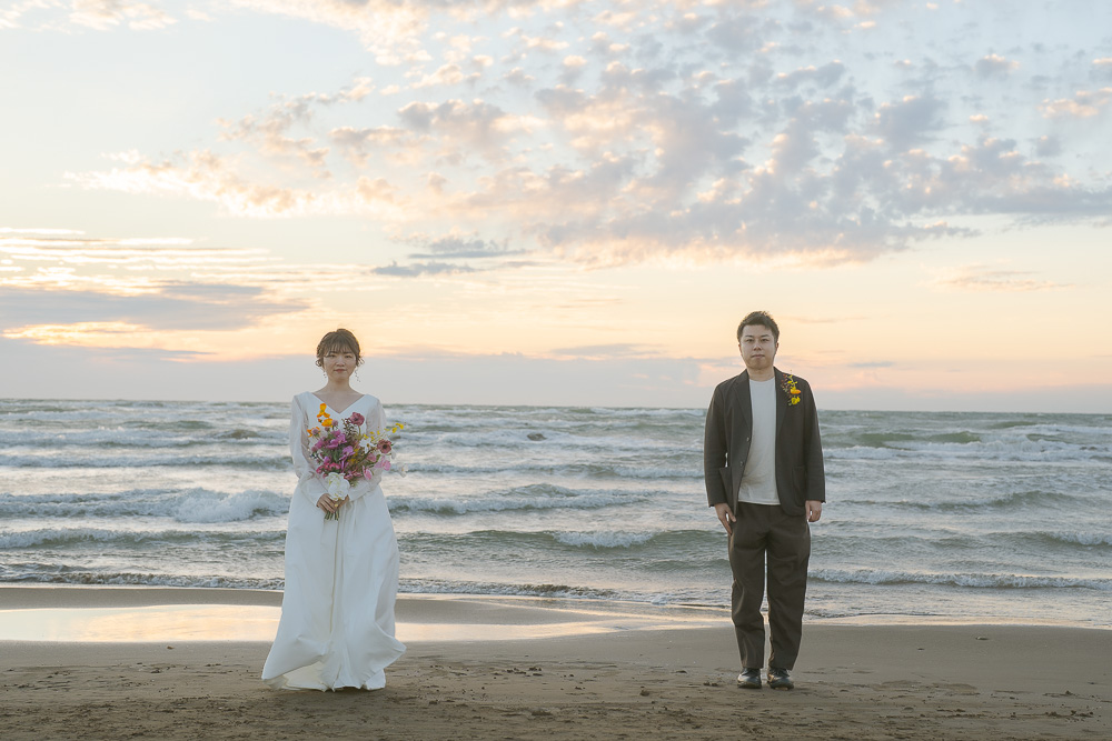 日が沈む海辺に立つ新郎新婦