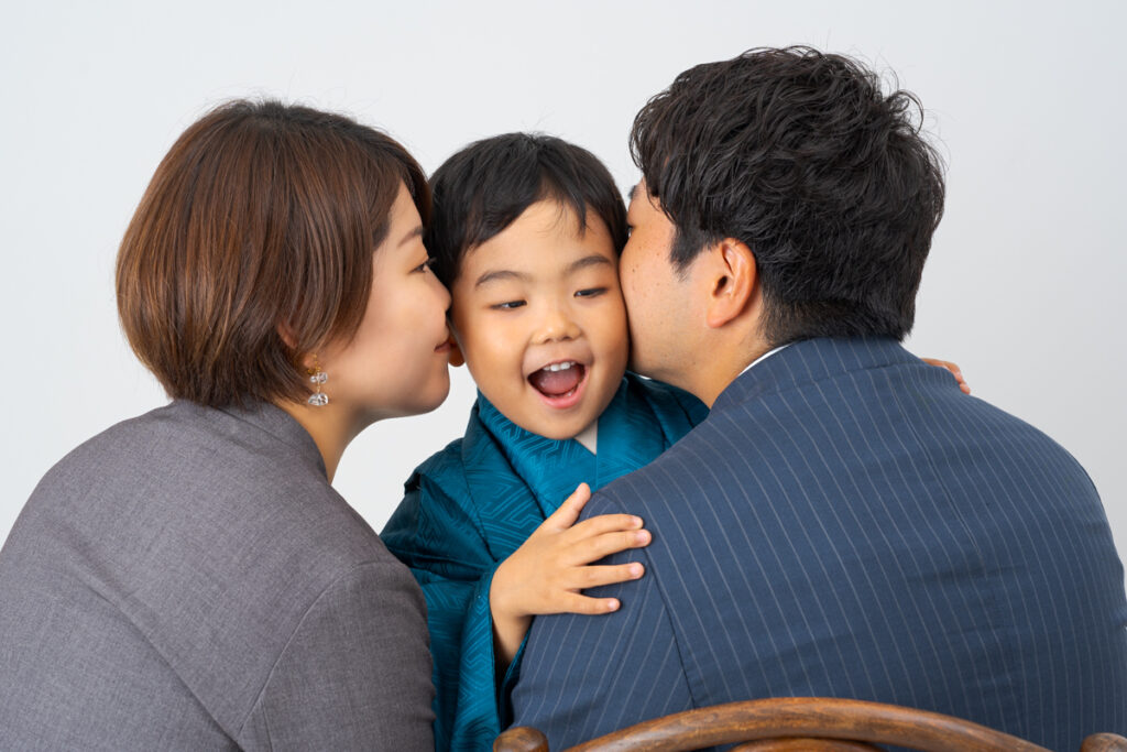 七五三の着物を着て、パパママに挟まれキスされる男の子