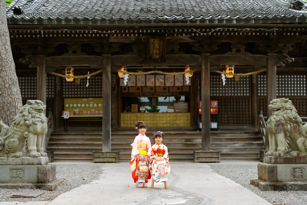 神社の前で椅子に座って七五三の記念写真を撮る姉妹