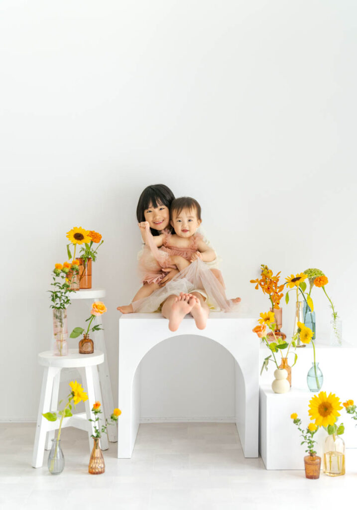 白い背景でひまわりに囲まれた仲良し姉妹の幸せポートレート