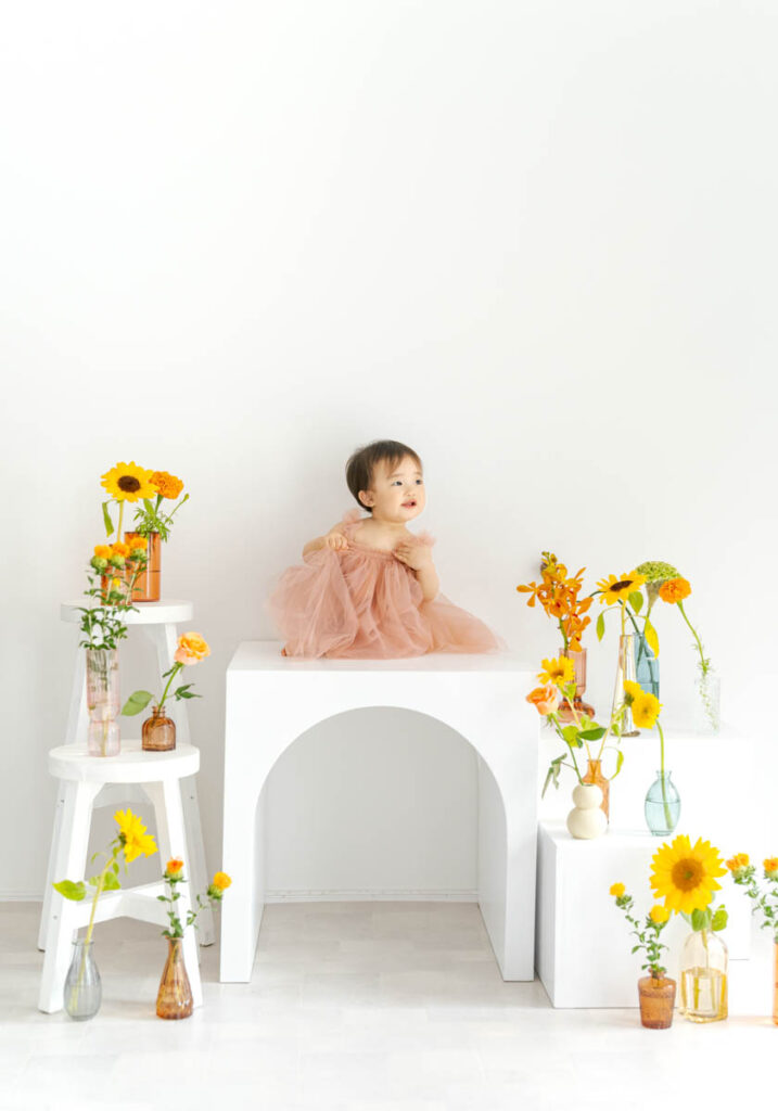 白い台に座るピンクチュチュの女の子と色鮮やかな花々