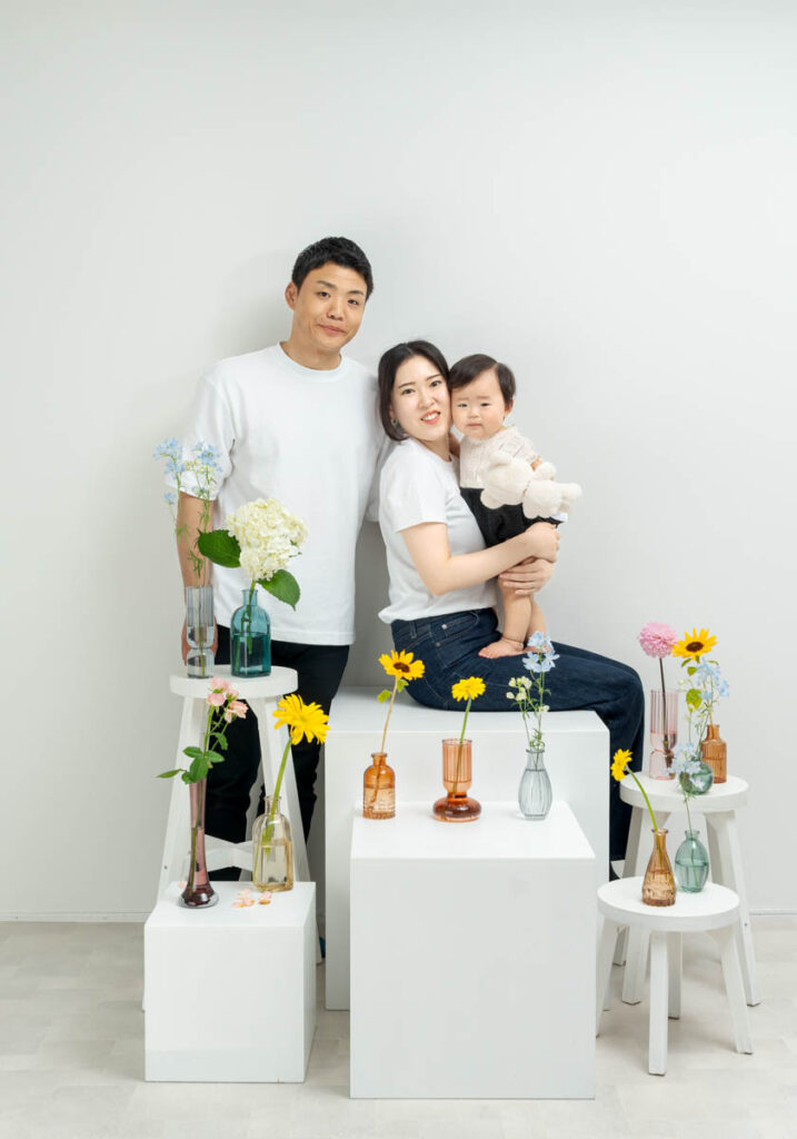 白い背景と花に囲まれた笑顔あふれる家族ポートレート