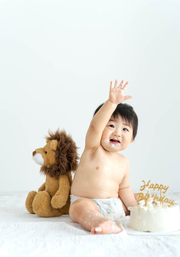 笑顔の赤ちゃんとライオンぬいぐるみの初誕生日ケーキ写真