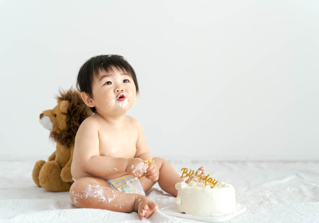 1歳の誕生日ケーキを楽しむ赤ちゃんとぬいぐるみの微笑ましい瞬間