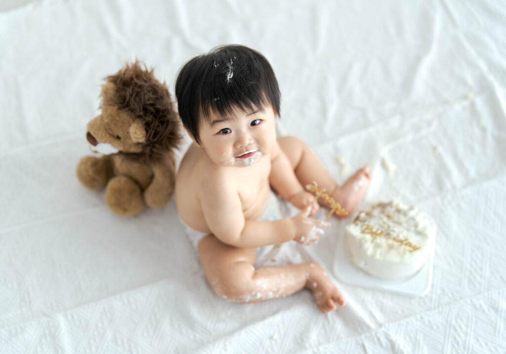 笑顔の赤ちゃんとライオンぬいぐるみの可愛いファーストバースデーケーキ写真