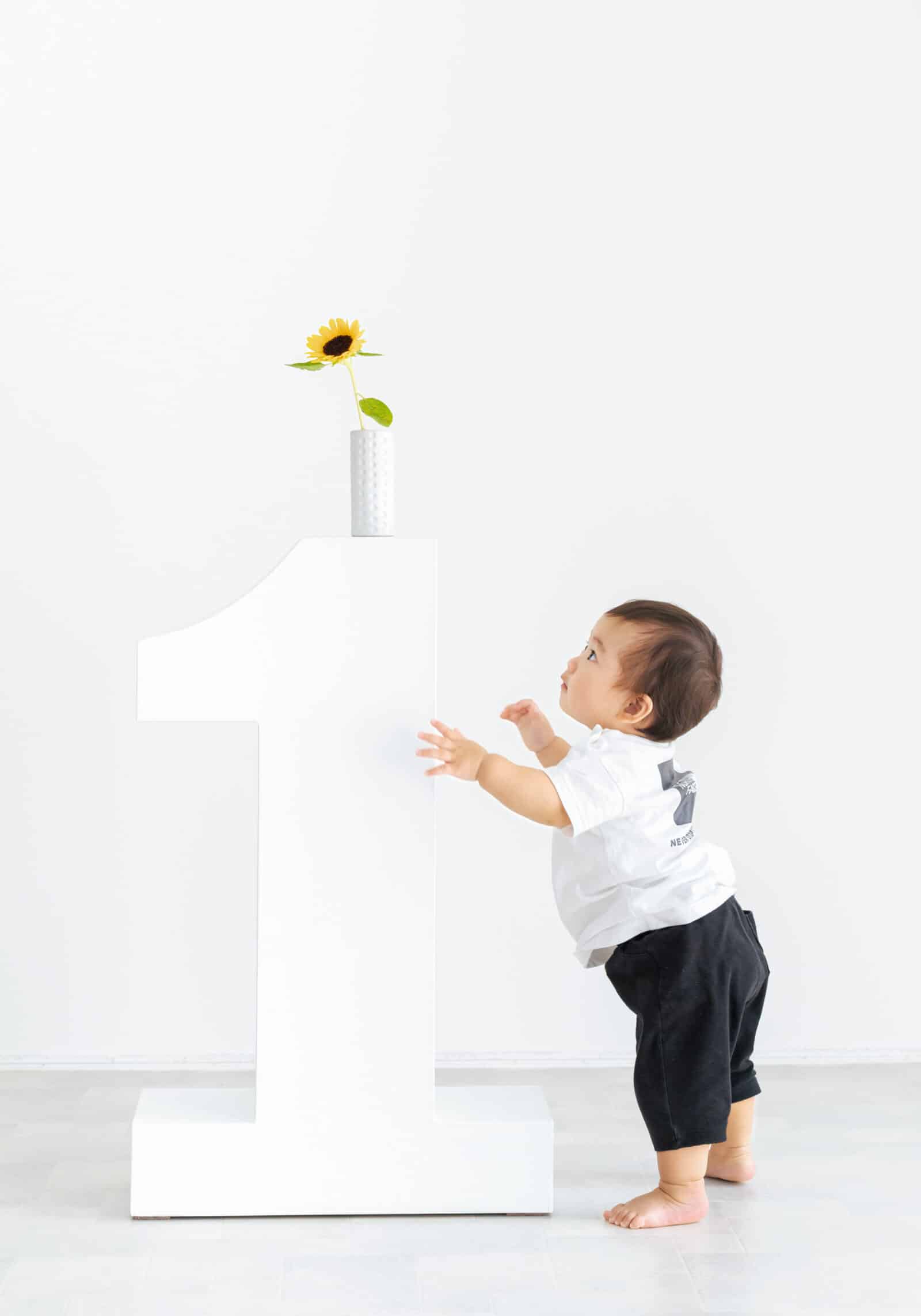 白い数字の1とひまわりに寄り添う1歳の誕生日フォト