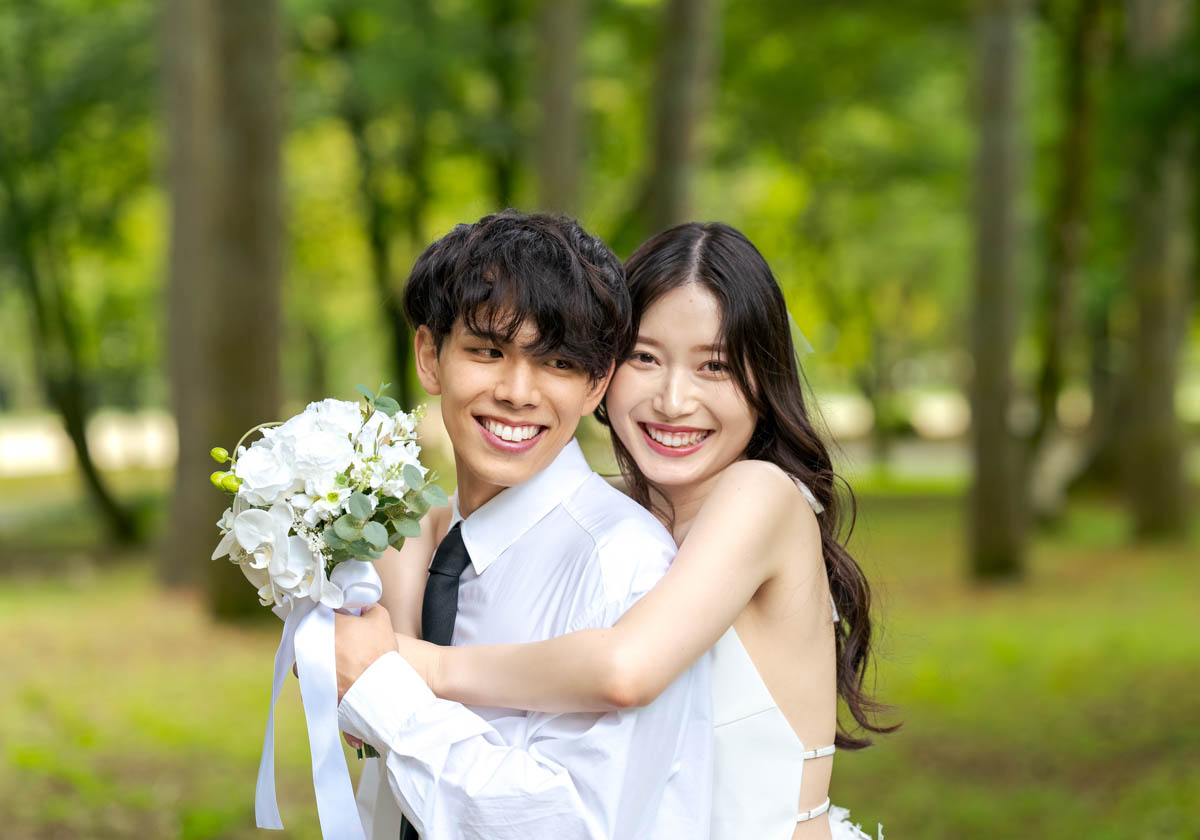 緑の公園で寄り添う笑顔のカップルのウェディング写真