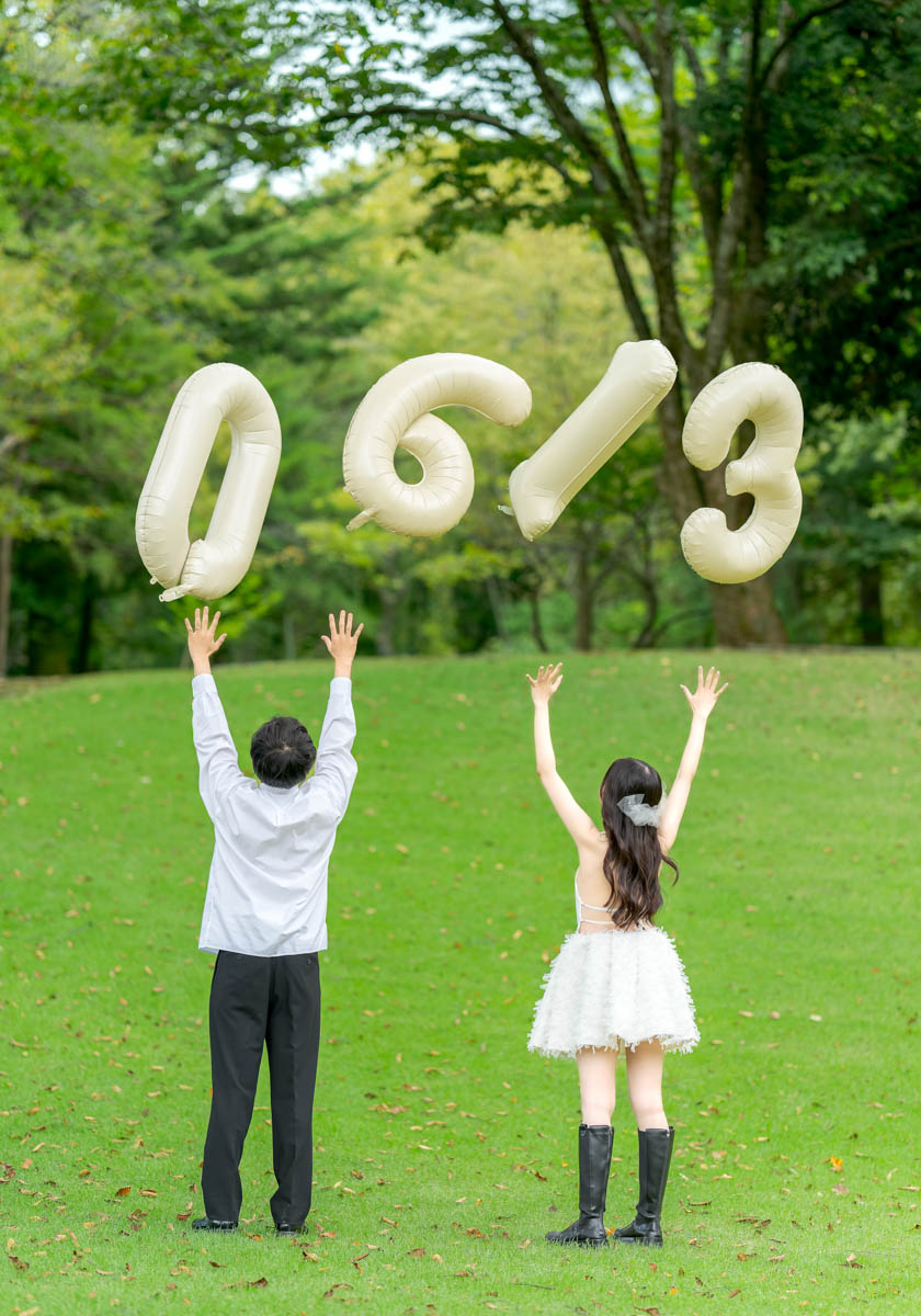 緑の公園で風船を掲げるカップルの記念日写真