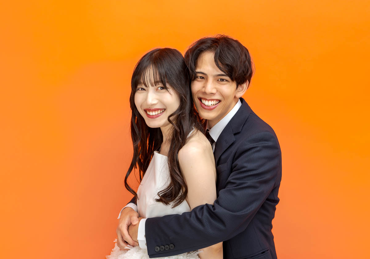 オレンジ背景で寄り添う笑顔のカップルの幸せな瞬間