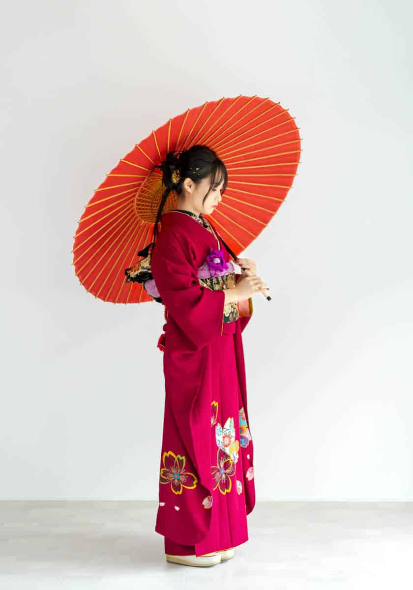 赤い着物と橙色の和傘を持つ優雅な日本女性の伝統的ポートレート