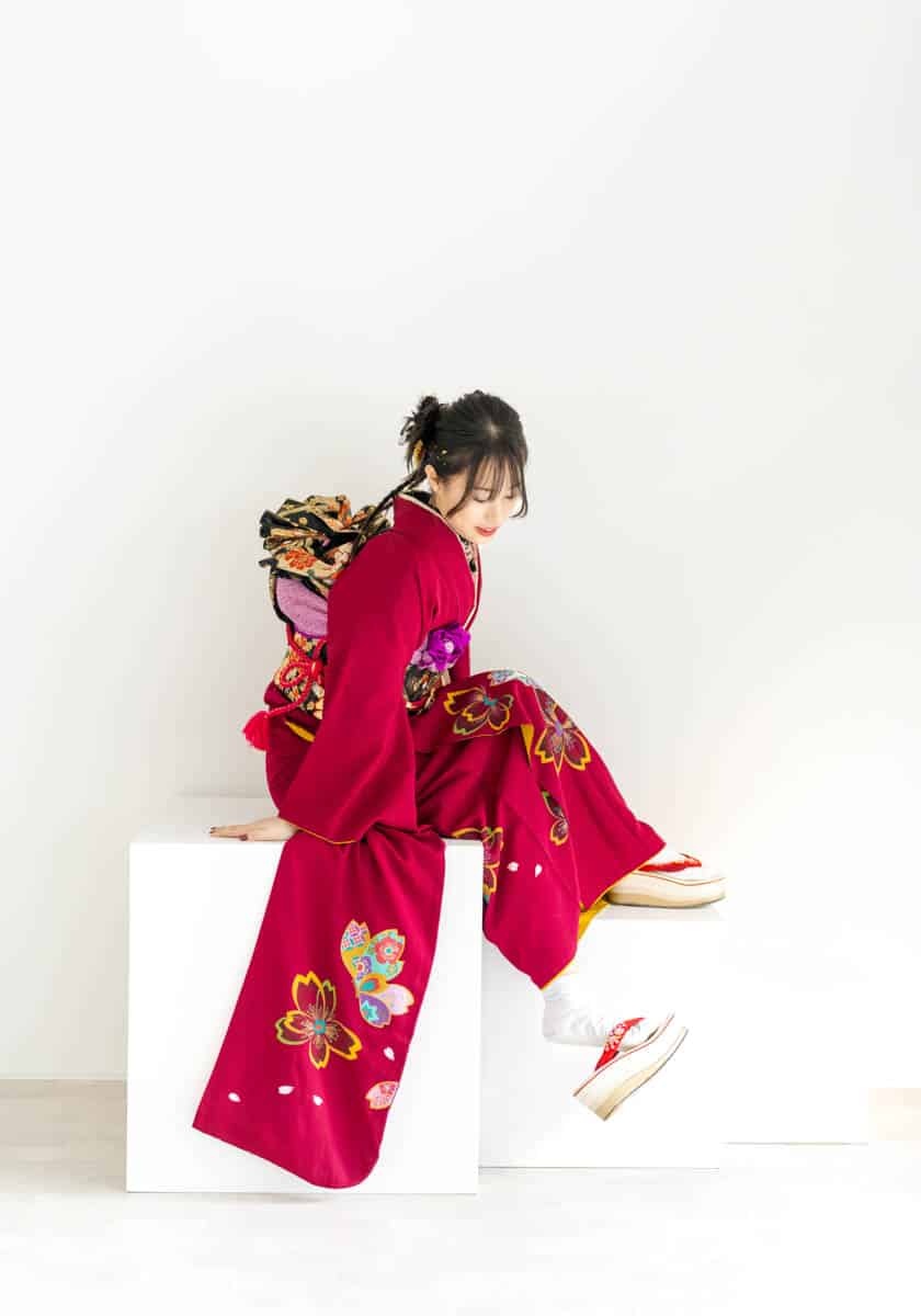 赤い着物を纏う女性が白背景で優雅に微笑む姿